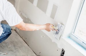 An image of a Man spackling new drywall or plasterboard. Home Living Construction will take care of all repairs after mold has been removed.