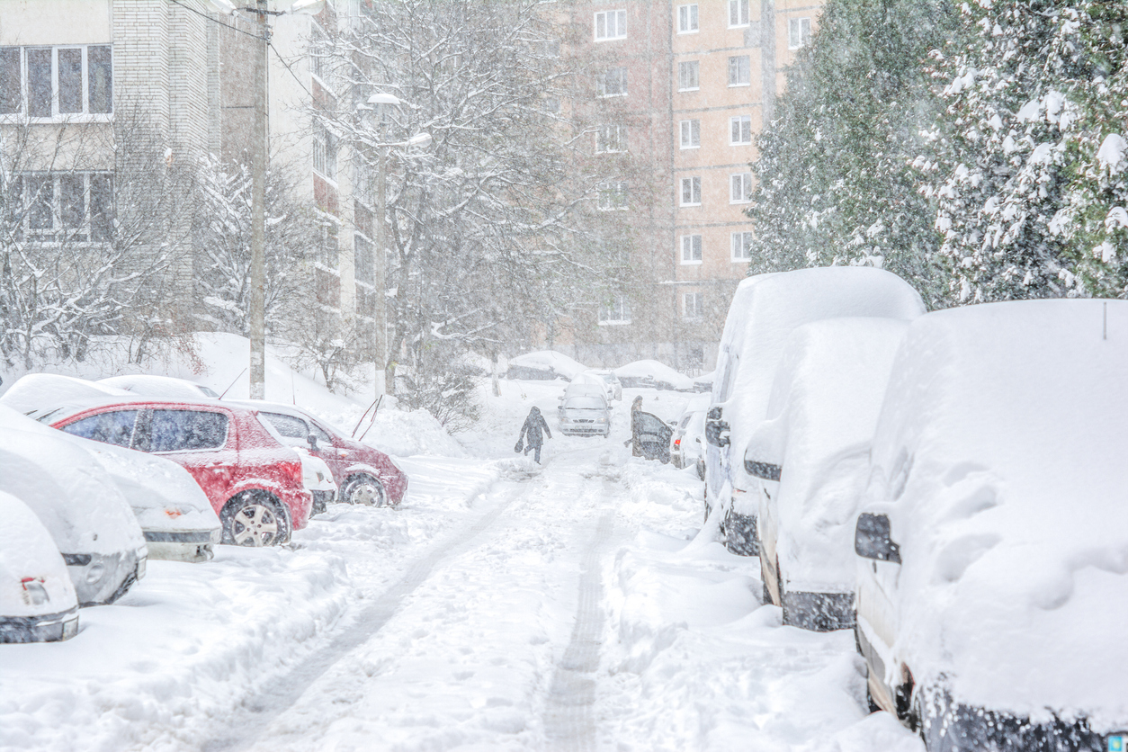 Snow-covered street and cars with a lonely pedestrian. Heavy snowstorm